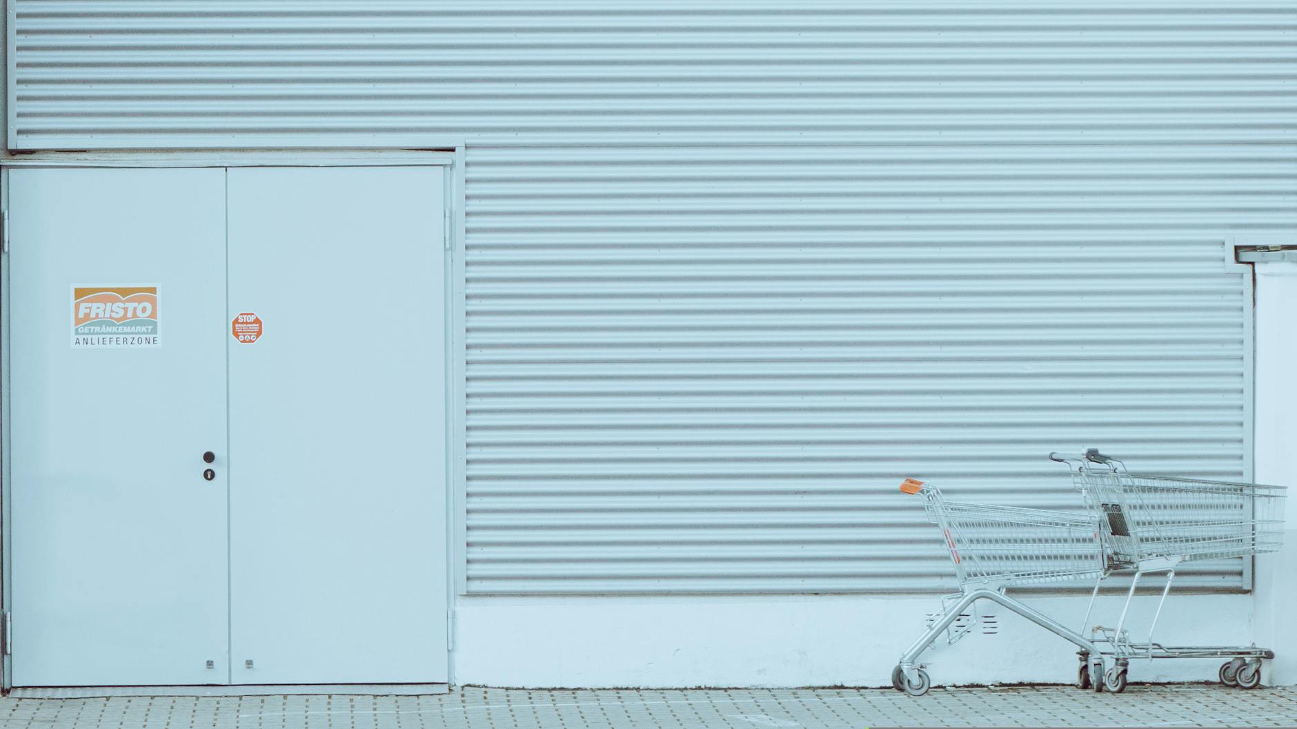 A minimalist urban setting featuring a turquoise corrugated wall and an empty shopping cart.