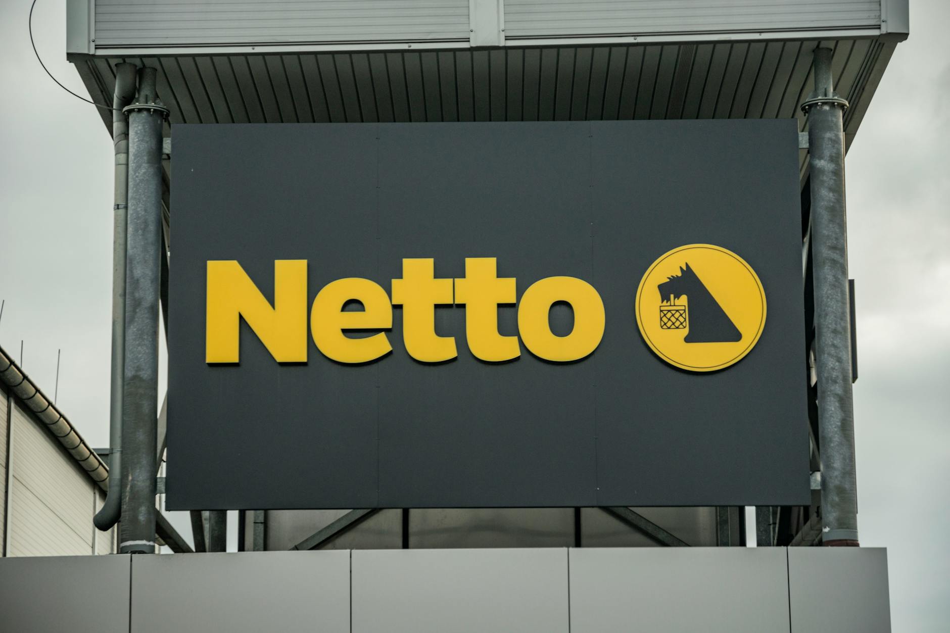 Exterior view of Netto supermarket branding, featuring yellow logo on dark background.