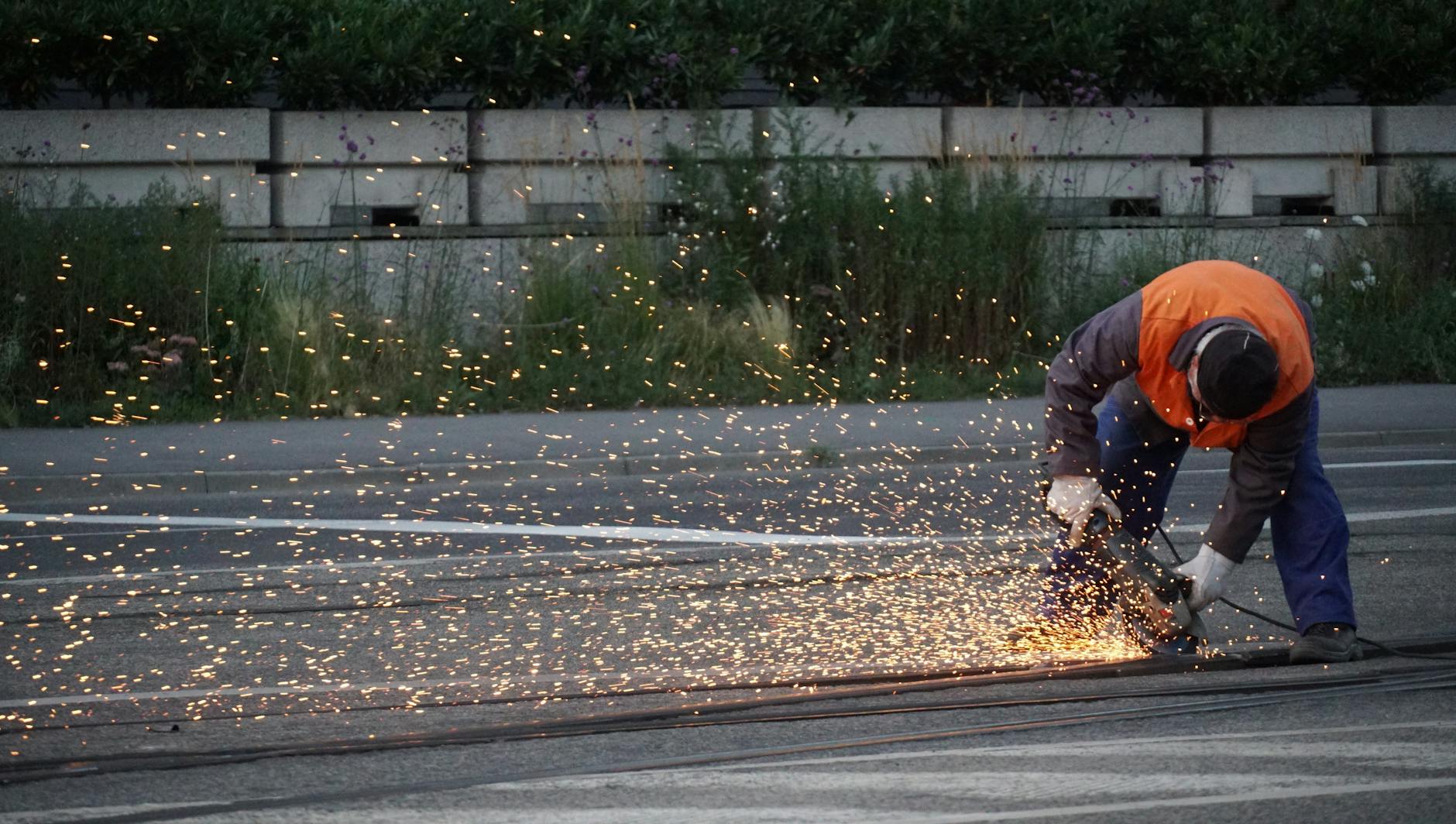A worker cuts railway tracks with a power tool, creating vivid sparks outdoors.