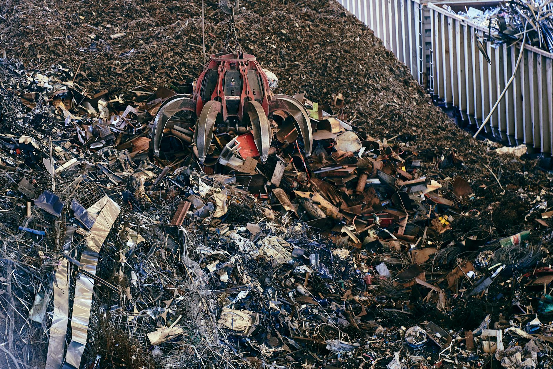 A claw excavator sifting through a large pile of industrial scrap metal outdoors.