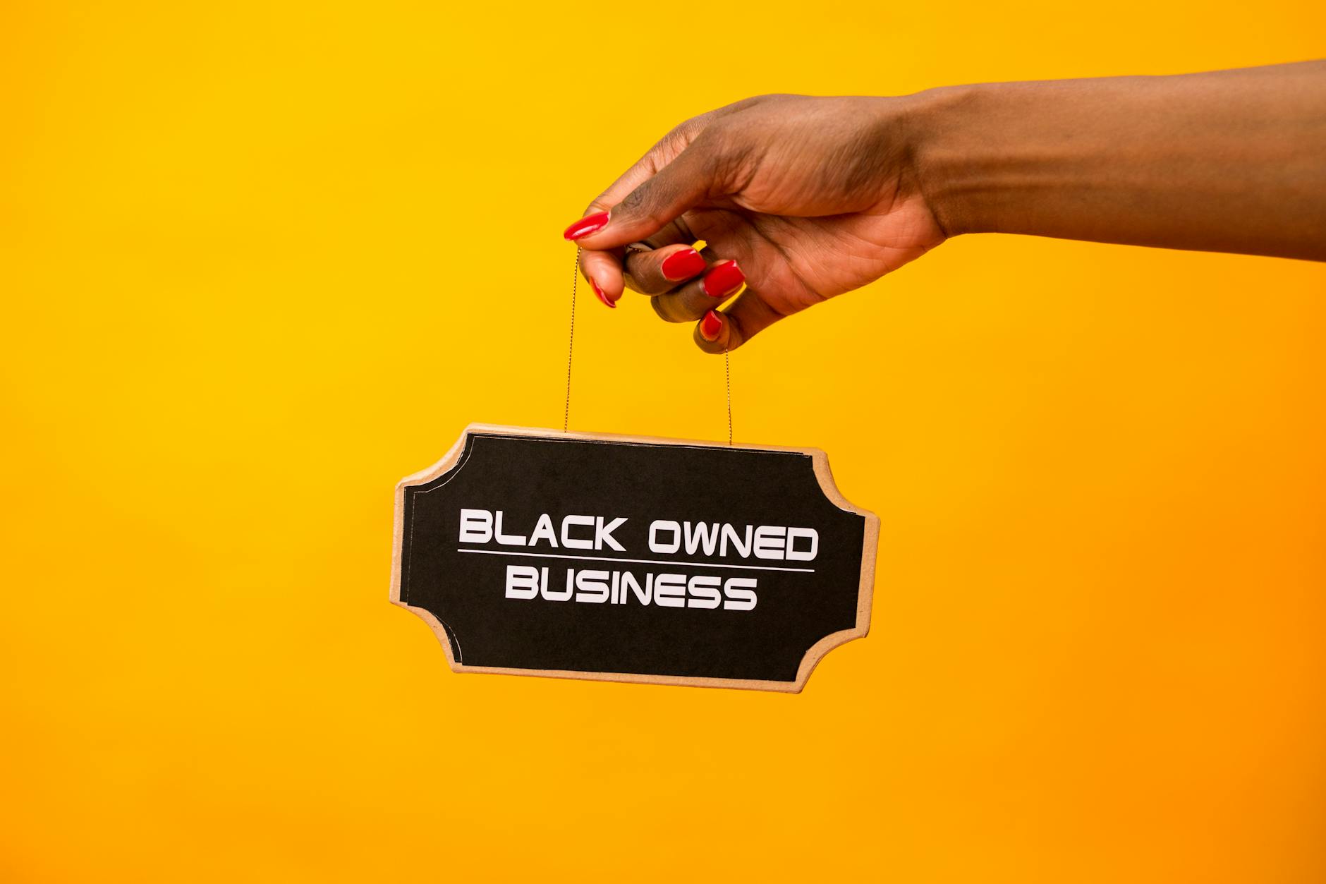 A hand holds a black owned business sign against a vibrant yellow background, symbolizing entrepreneurship.
