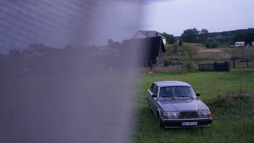Silver volvo parked in a grassy field near houses.
